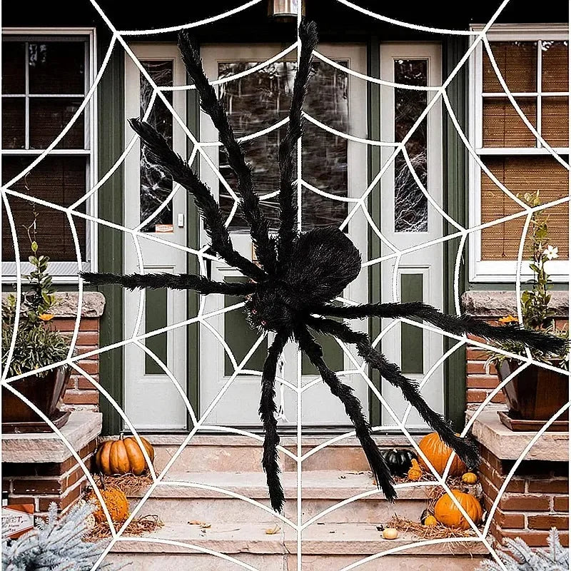 Large decorative spider on a spider web with pumpkins and festive decorations outside a house.