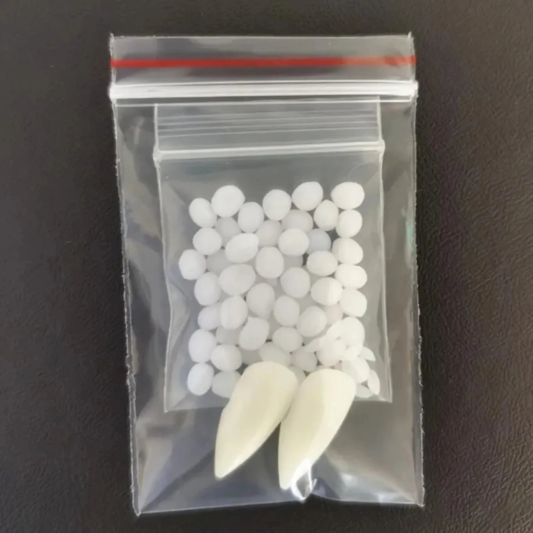 Clear plastic bag with white spherical objects and two large white objects on a dark background