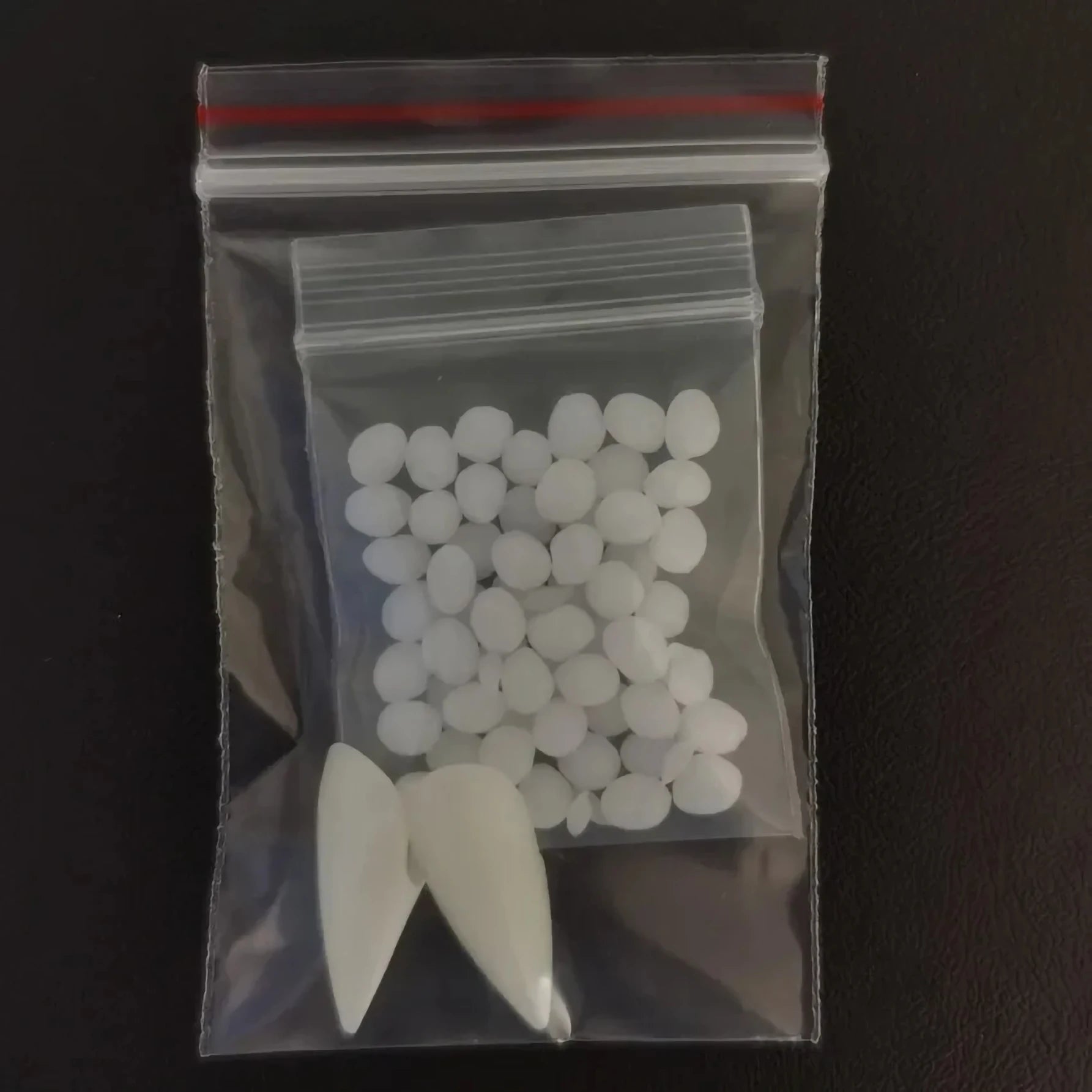 Clear plastic bag with white pills and a small white object on a dark background