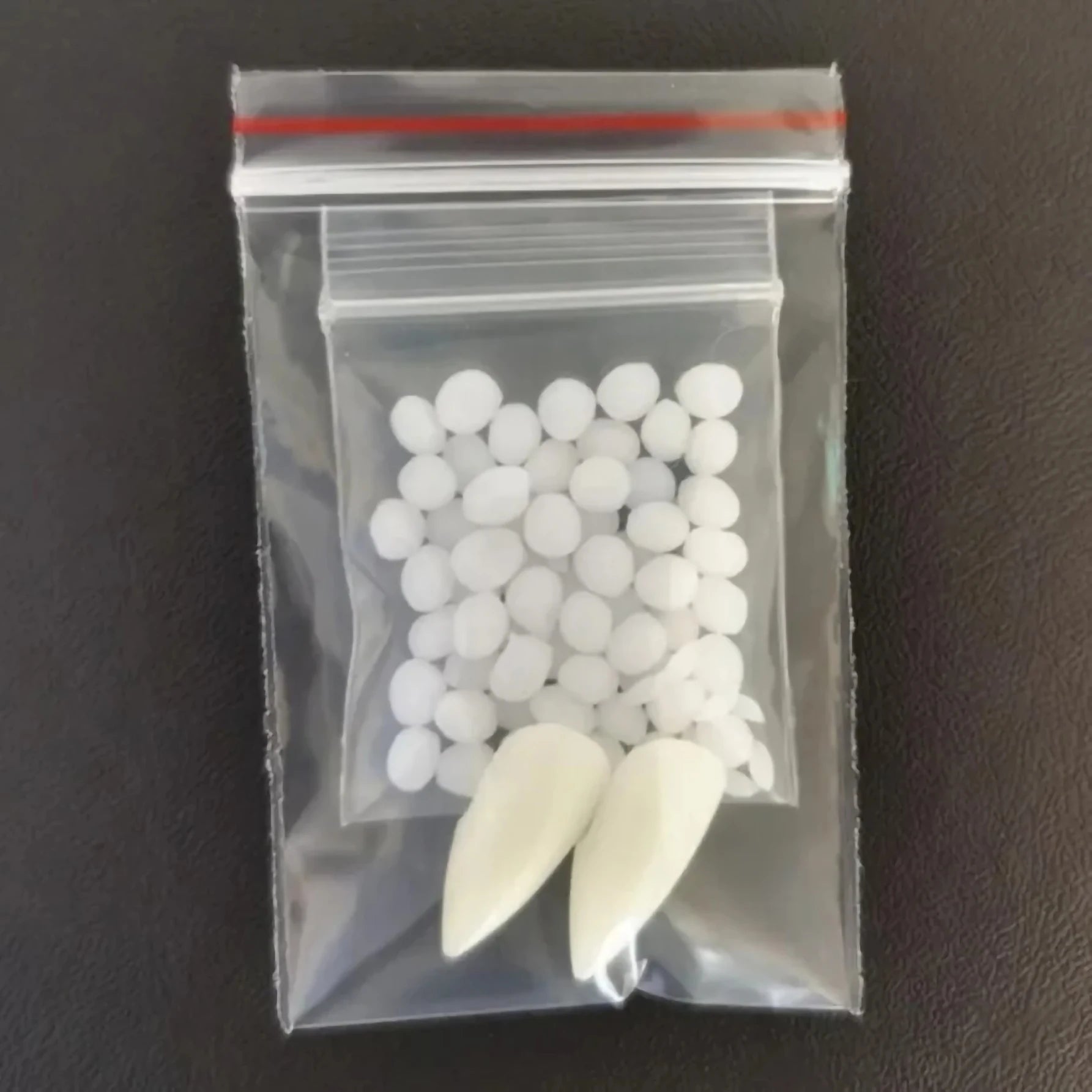 Clear plastic bag with white spherical objects and two large white cones on a dark surface